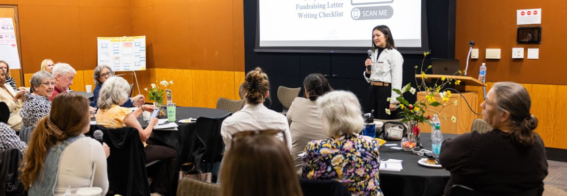 A speaker holds a microphone and addresses an audience at the 2025 Lab iMPACTLY Nonprofit Workshop.