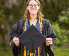 Chloe Lemos, a senior criminal justice major, stands in her cap and gown apparel with five cords at the Founders Bell Pavilion April 13. (Sydney Willis)