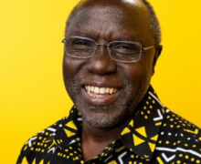 Dr. Jesse Lutabingwa is a professor of public administration in Appalachian State University's Department of Government and Justice Studies. Photo by University Communications Smiling man with glasses and a beard, wearing a black shirt patterned with yellow geometric shapes against a bright yellow background.